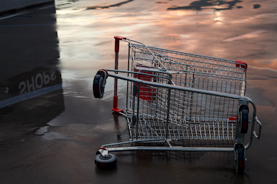 shopping trolley tipped over with shops sign reflected on the wet ground.